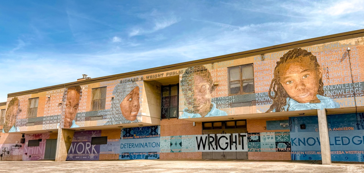 Exterior view of Richard R. Wright School featuring a large colorful mural with student portraits and inspirational words including “Work,” “Determination,” and “Knowledge” across the front of the school building.